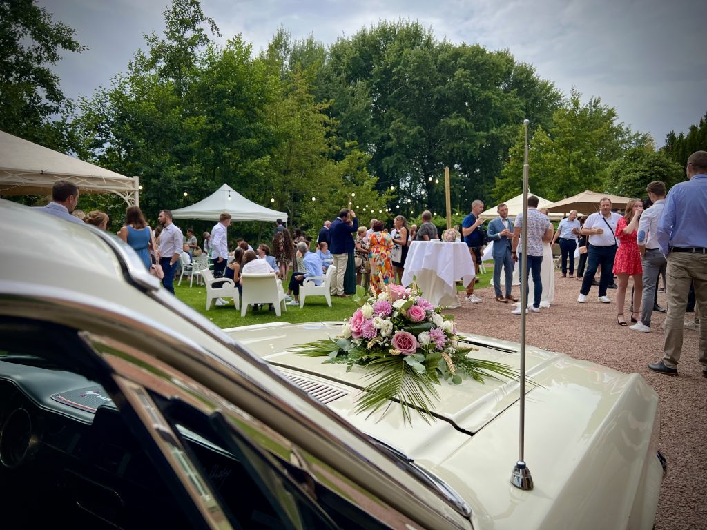 Cérémonie de mariage en plein air au style vintage, avec une voiture ancienne décorée, entourés de leurs invités dans un cadre romantique.