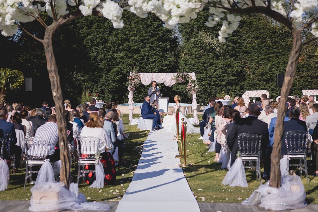 Cérémonie de mariage en plein air avec des mariés échangeant leurs vœux devant un décor floral et une assemblée d'invités.